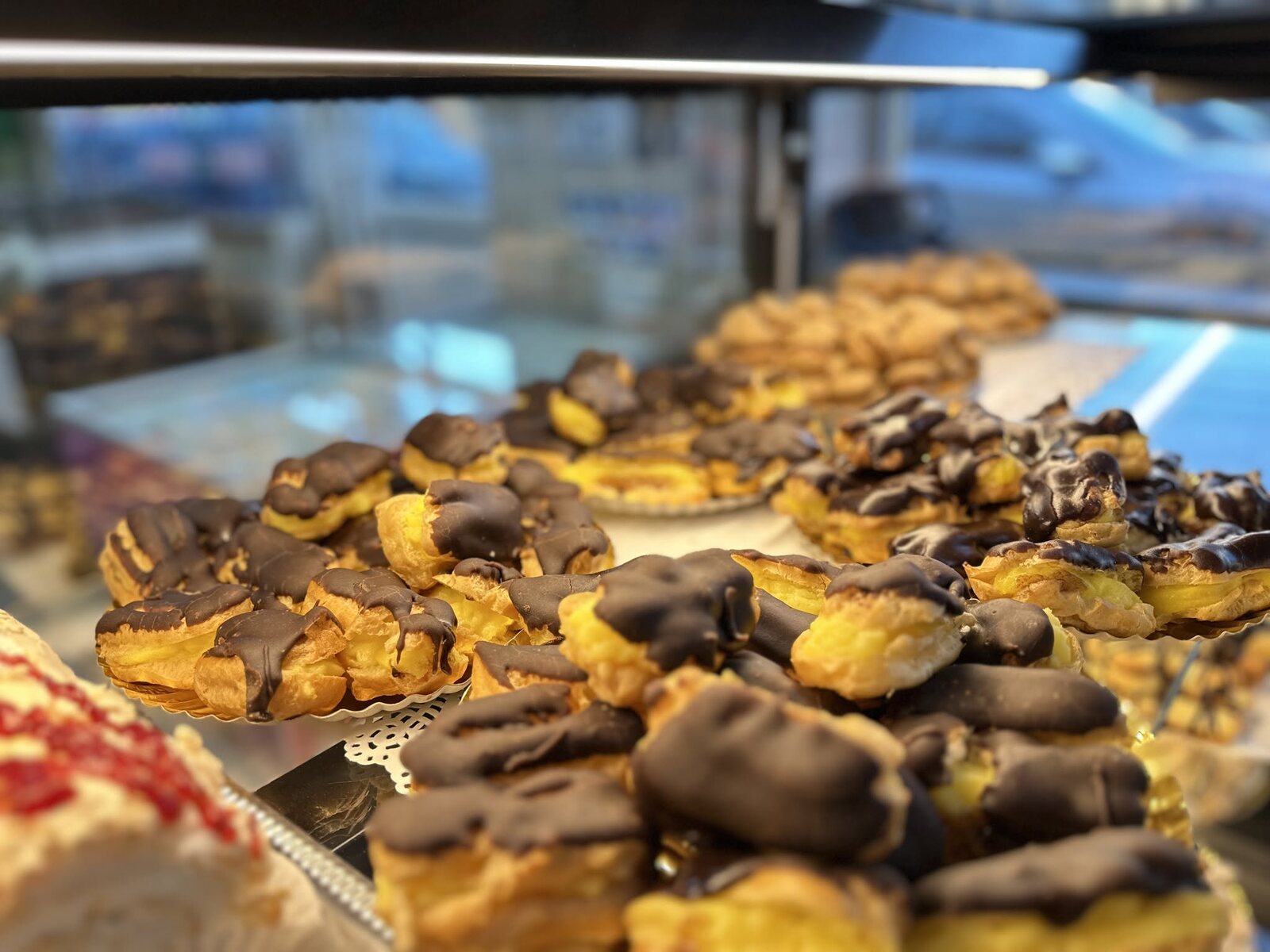 Choux și eclere cu glazură de ciocolată, pe tăvi în vitrină